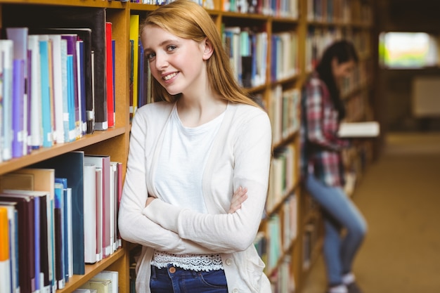 Glimlachende student die tegen boekenplanken leunt