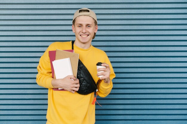 Glimlachende student in een geel sweatshirt en pet staat