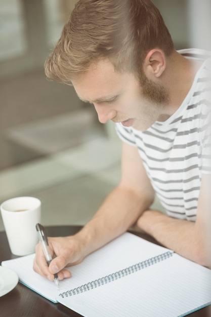 Foto glimlachende studentenzitting met een hete drank en het schrijven op blocnote