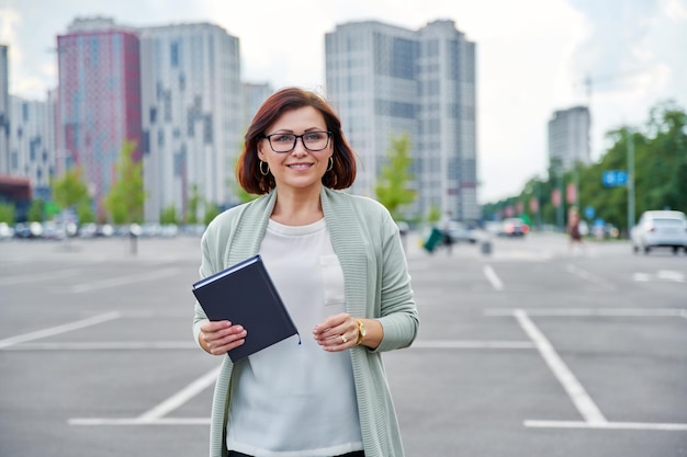 Glimlachende succesvolle rijpe bedrijfsvrouw die openlucht moderne stedelijke stijlachtergrond lopen