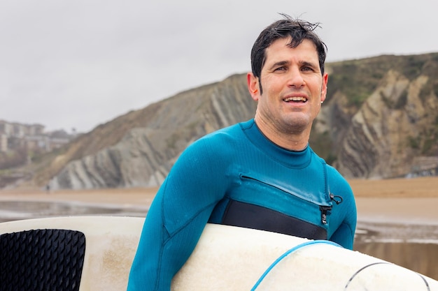 Glimlachende surfer bij de zee met kliffen op de achtergrond