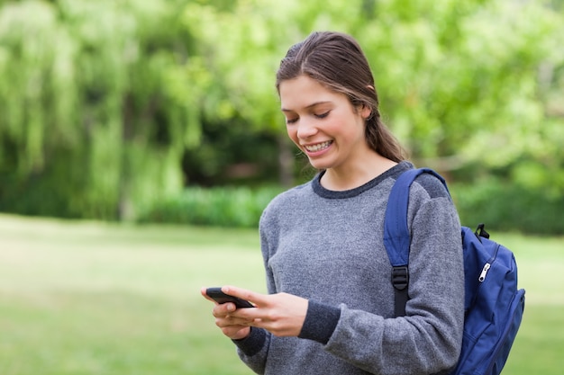 Glimlachende tiener die haar cellphone gebruikt terwijl het ontvangen van een tekst