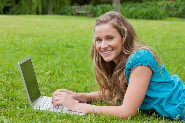 Glimlachende tiener die haar laptop met behulp van terwijl het liggen in een park