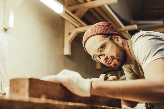 Glimlachende timmerman die met houten plank werkt