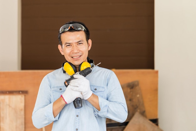 Glimlachende timmerman met elektrische schroevendraaier in de werkplaats Technische man die houtwerk doet in timmerwerk