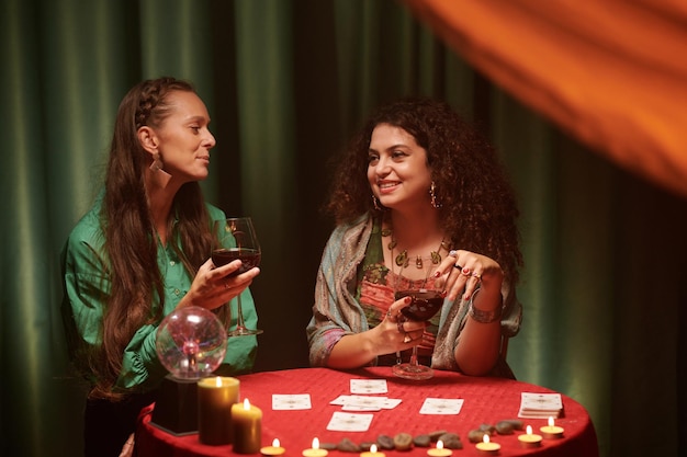 Glimlachende toekomstige tellers drinken wijn en verspreiden tarotkaarten.