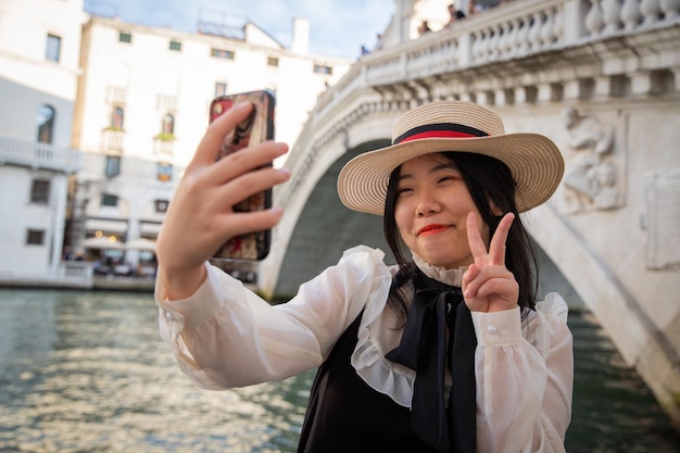 Glimlachende toerist doet het V-teken van overwinning onder de Rialtobrug in Venetië terwijl hij een selfie maakt
