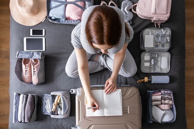 Glimlachende toeristenvrouw die koffer inpakken aan vakantiebriefpapierlijst die zich klaar maken om reis te reizen