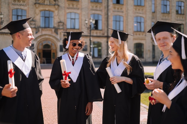 Glimlachende universitair afgestudeerden die op de campus staan en elkaar feliciteren voordat ze vertrekken