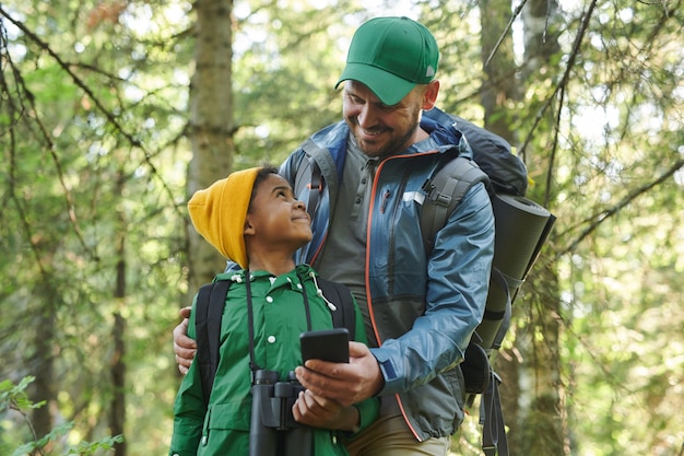 Glimlachende vader die iets toont aan zijn zoon op mobiele telefoon tijdens hun wandeling in het bos