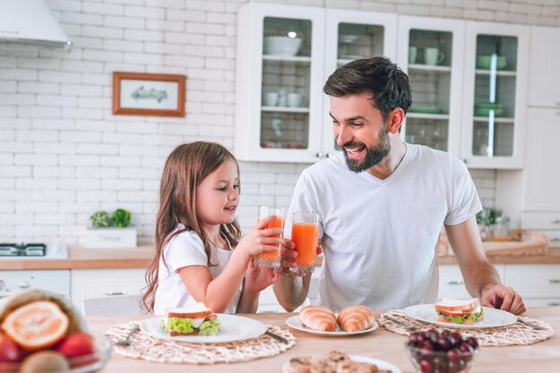 Glimlachende vader en dochter klikkende glazen met het drinken van sap voor ontbijt in de keuken