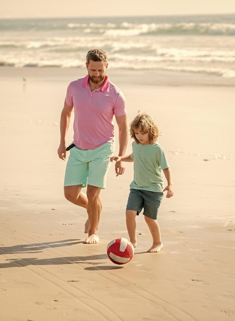 Glimlachende vader en zoon voetballen op zomerstrand met bal vaderdag