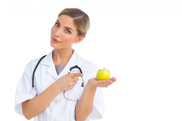 Glimlachende verpleegster die aan groene appel op haar hand richt