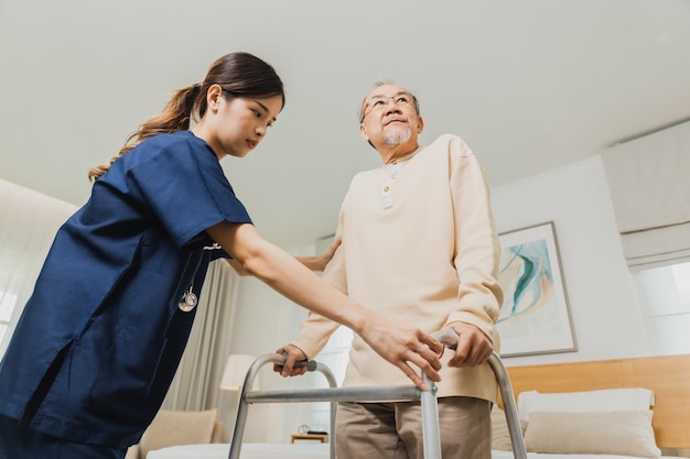 Glimlachende verpleegster helpt een oudere Aziatische man om rond te lopen in het verpleeghuis gebruik een wandelstoel met een sterke gezondheid en Help en zorg concept