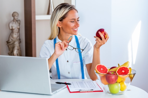 Glimlachende voedingsdeskundige die in bureau een fruit houdt