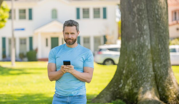 Glimlachende volwassen man die buiten in huis staat te chatten via de telefoon, online kopen