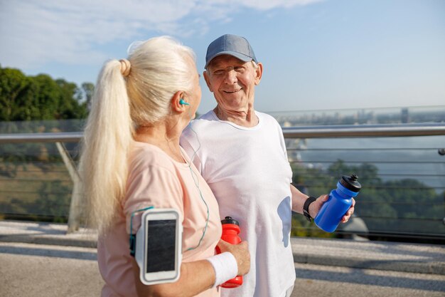 Glimlachende volwassen man en vrouw met fles water bij training op voetgangersbrug