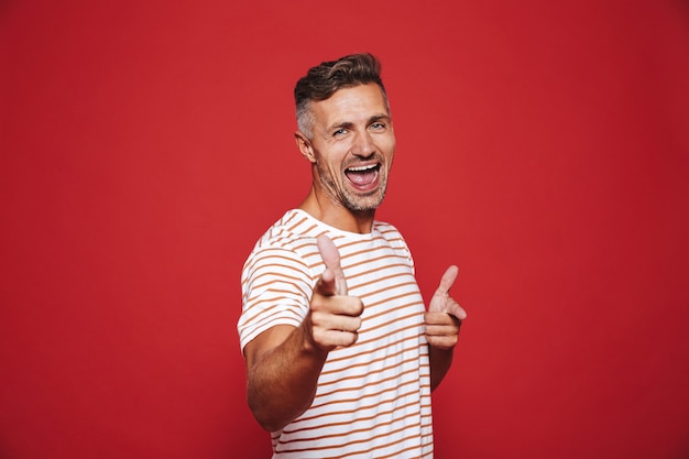 Glimlachende volwassen man in gestreept t-shirt gebaren wijsvinger, wat betekent dat je geïsoleerd op rood