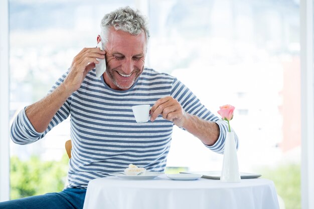 Glimlachende volwassen man praten over de telefoon terwijl het hebben van koffie