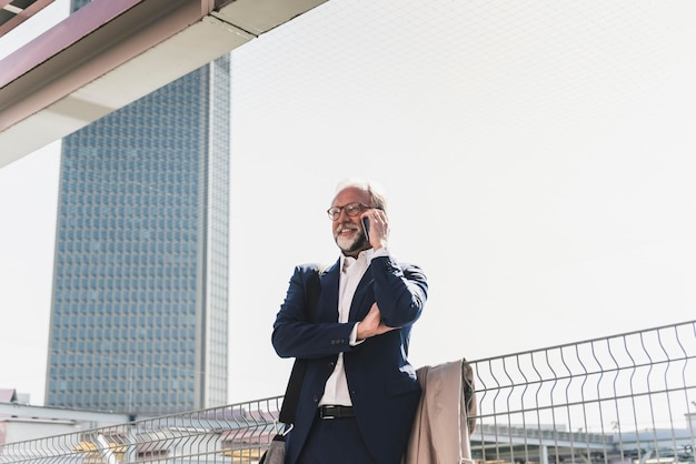 Glimlachende volwassen zakenman in de stad op mobiele telefoon