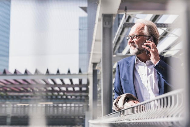 Glimlachende volwassen zakenman in de stad op mobiele telefoon