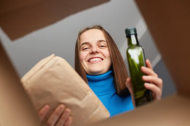 Glimlachende vriendelijke charmante vrouw die in de doos kijkt, vrijwilliger die voedseldonaties inzamelt voor de behoeften van Oekraïense migranten die boodschappen doen, de bestelling van boodschappen ontvangen