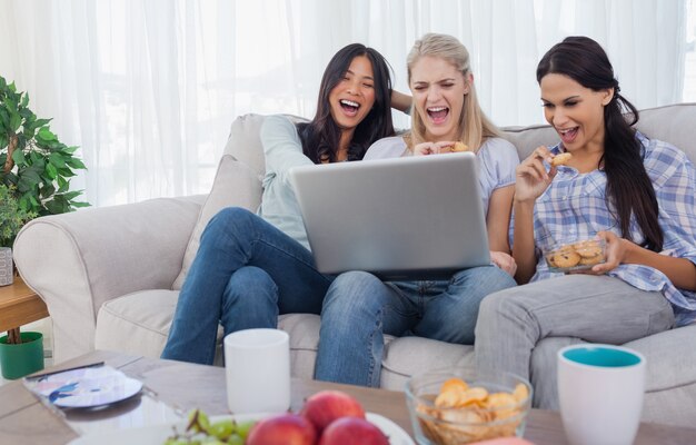 Glimlachende vrienden die laptop samen bekijken en koekjes eten