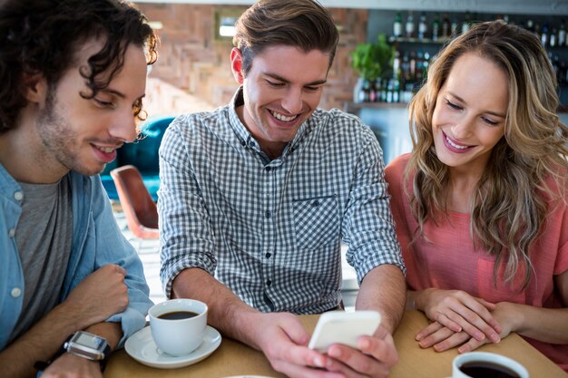 Glimlachende vrienden die mobiele telefoon met behulp van