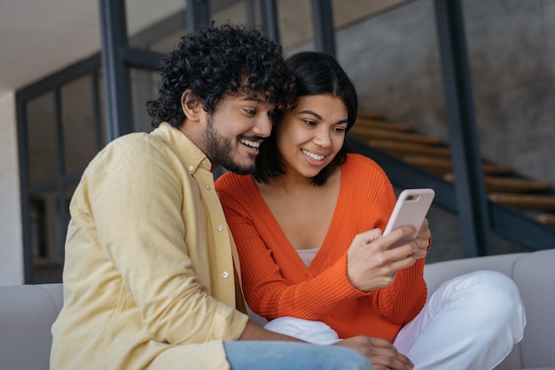 Glimlachende vrienden die mobiele telefoons gebruiken om online te winkelen en een mobiel spel te spelen dat thuis ontspant