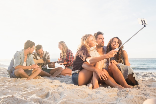 Glimlachende vrienden die op zand zitten en selfies nemen