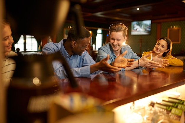 Glimlachende vrienden vrije tijd aan het loket in de bar. Groep mensen ontspannen in pub, nachtlevensstijl, vriendschap, evenementviering