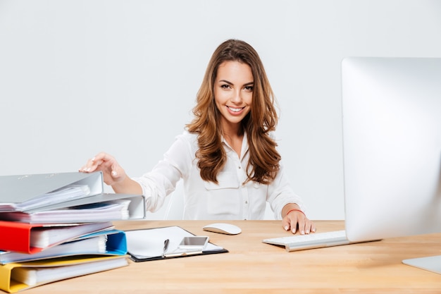 Glimlachende vrolijke zakenvrouw zittend op haar werkplek isoltaed op de witte achtergrond
