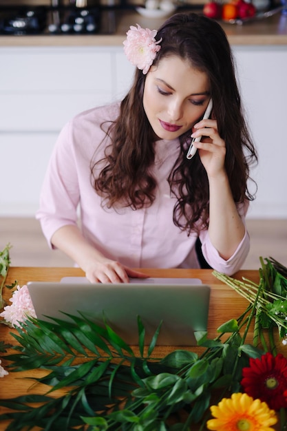 Glimlachende vrouw bloemist klein bedrijf eigenaar bloemenwinkel ze gebruikt haar telefoon en laptop om bestellingen op te nemen voor haar online winkel thuiswerken