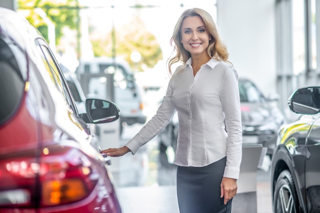 Glimlachende vrouw die autodeur in dealer aanraakt