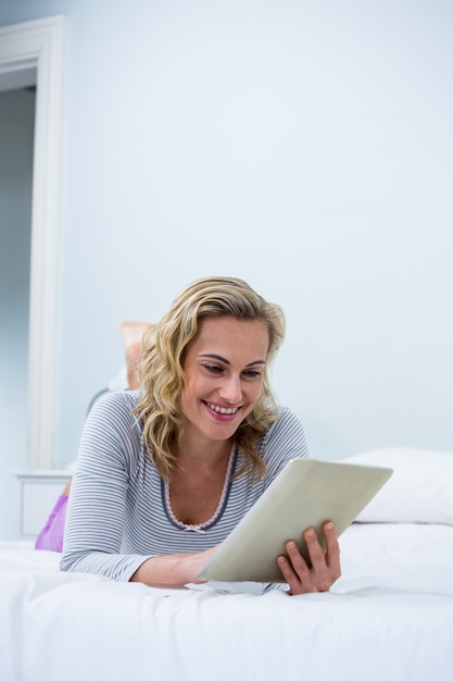 Glimlachende vrouw die digitale tablet op bed gebruiken