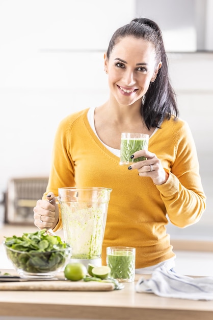 Glimlachende vrouw die een glas spinazie groene smoothie houdt