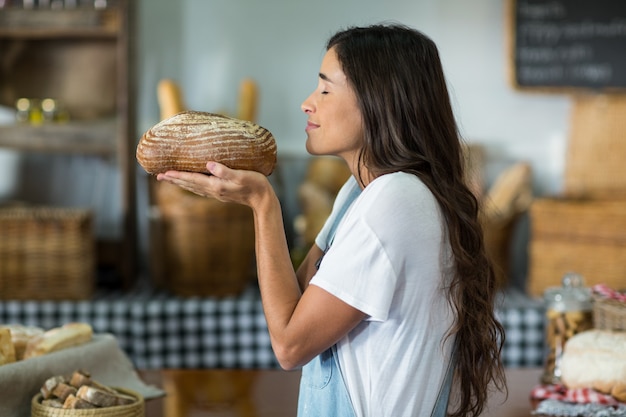 Glimlachende vrouw die een rond brood aan balie ruikt