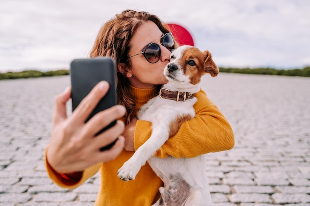 Glimlachende vrouw die een selfie maakt terwijl ze buiten met een hond staat