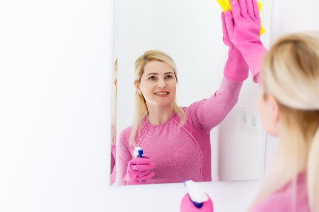 Glimlachende vrouw die een spiegel in een badkamer thuis schoonmaakt