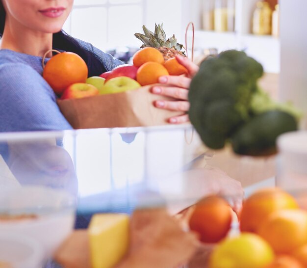 Glimlachende vrouw die een vers fruit uit het koelkastconcept voor gezond eten haalt