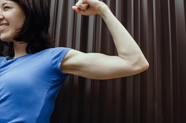 Glimlachende vrouw die haar bicepsen in openlucht buigt,