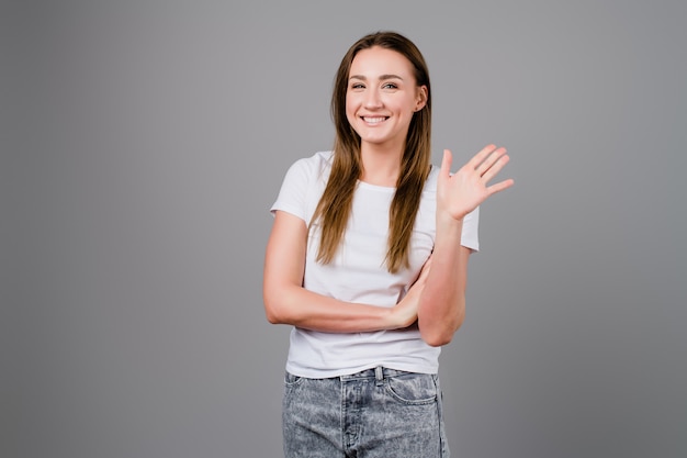 Glimlachende vrouw die hello met hand golven die op grijs wordt geïsoleerd