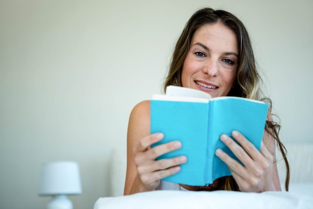 glimlachende vrouw die in bed ligt die een boek leest