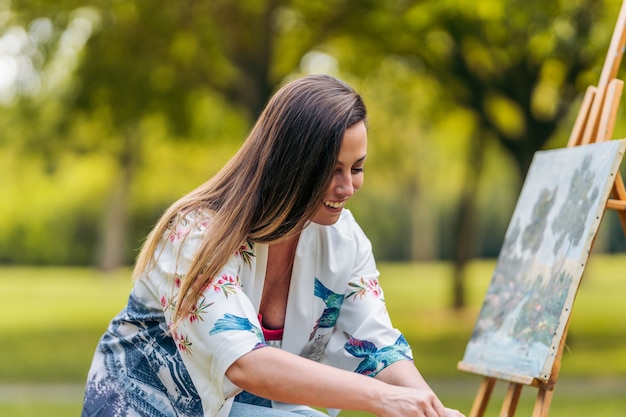 Glimlachende vrouw die in een park zit voor een canvas dat pijn doet