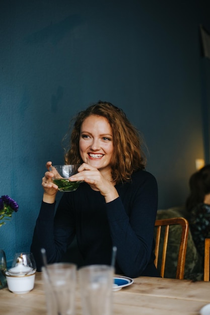 Glimlachende vrouw die kruidenthee vasthoudt terwijl ze in een café zit