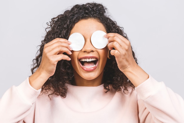 Glimlachende vrouw die make-up verwijdert. Foto van Afro-Amerikaanse vrouw houdt wattenschijfjes in de buurt van gezicht geïsoleerd op een witte achtergrond. Huidverzorging en beauty concept.