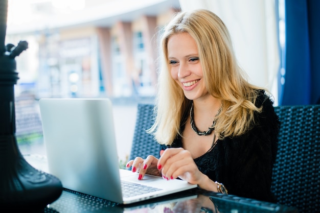 Glimlachende vrouw die met laptop werken openlucht bij koffie