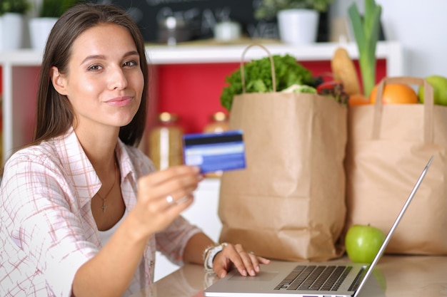 Glimlachende vrouw die online winkelt met tablet en creditcard in de keuken Glimlachende vrouw