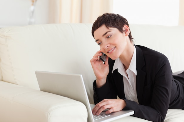 Glimlachende Vrouw die op een bank met laptop en een telefoon ligt