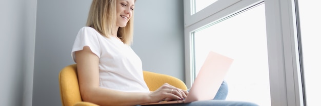 Glimlachende vrouw die op laptop werkt terwijl ze in de stoel zit